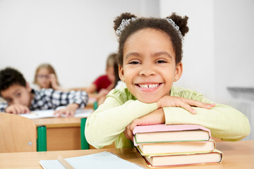 Front view of happy african girl lying on books and laughing