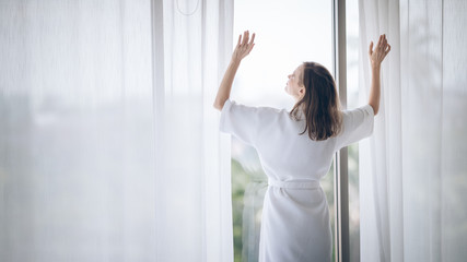 Attractive woman gesture happy when she woke up and got out, opened the curtains at the window