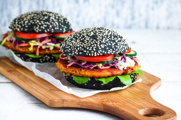 homemade vegan burgers with black bun carrot cutlet coleslaw salad cucumber tomato on cutting board