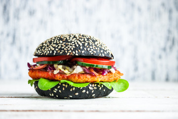 healthy vegan burger with black bun carrot cutlet coleslaw salad cucumber tomato on wooden table