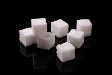 Sugar cubes on a black background. Cubes of sugar. Refined sugar on the black mirror surface of the table.