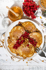 tasty pancakes with berries and honey on a white wooden table, vertical top view