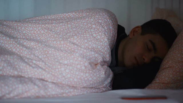 Young man waking up at night by cellphone on bed at home