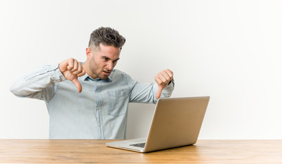 Young handsome man working with his laptop showing thumb down and expressing dislike. © Asier
