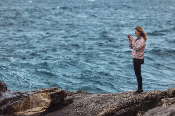 young woman in coat at seaside looking at storming sea