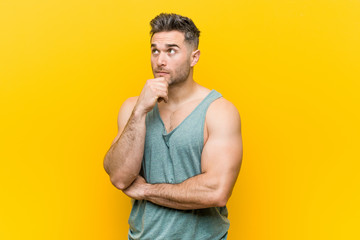 Young fitness man against a yellow background looking sideways with doubtful and skeptical expression. - obrazy, fototapety, plakaty