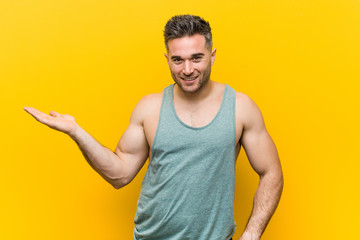 Young fitness man against a yellow background showing a copy space on a palm and holding another...