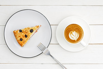Cup of coffee and piece of homemade cake with cottage cheese souffle decorated with almonds and blueberries on white wooden table. Top view.