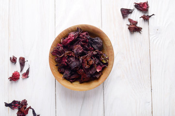 Top view at wooden bowl of dry hibiscus petals on white background