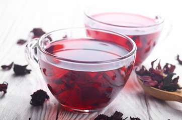 Closeup view at two tea cups and dry hibiscus petals on white wooden table background