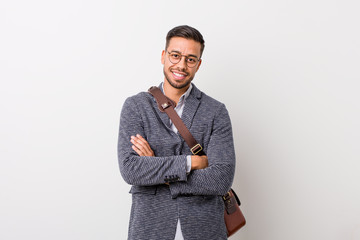 Young business filipino man against a white wall who feels confident, crossing arms with determination.