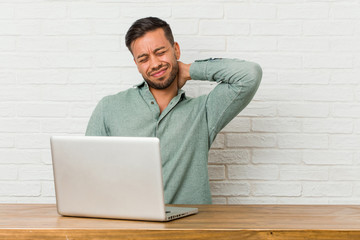 Young filipino man sitting working with his laptop suffering neck pain due to sedentary lifestyle.