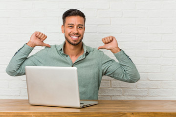 Young filipino man sitting working with his laptop feels proud and self confident, example to follow.