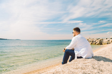 Naklejka na ściany i meble young stylish man sitting at sea beach enjoying the view