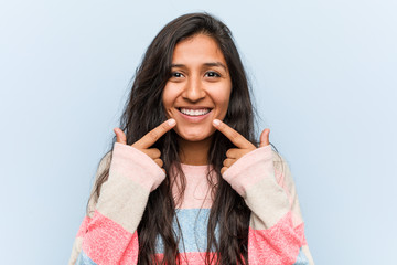 Young fashion indian woman smiles, pointing fingers at mouth.