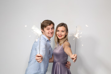 Party, celebration, event and holidays concept - man dressed in blue shirt and woman dressed in purple dress hold a firework stick