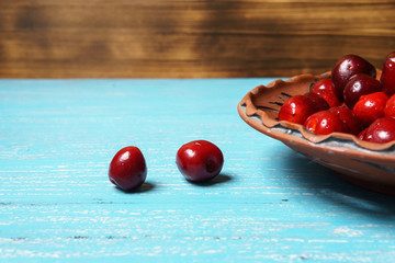 Red sweet cherry in a clay plate on a turquoise wooden table