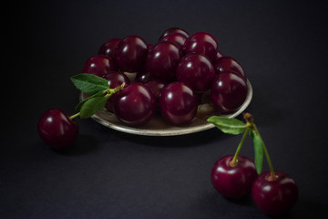Cherry berries in a small metal Cup and green stems on a black background