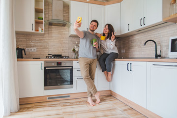 cheerful man with woman taking selfie on the kitchen while drinking tea