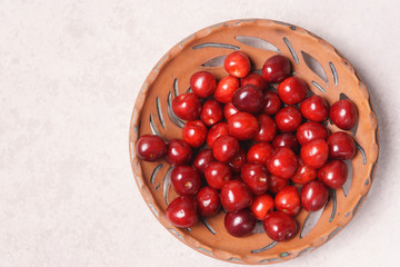 Red sweet cherry in a clay plate on a cream table