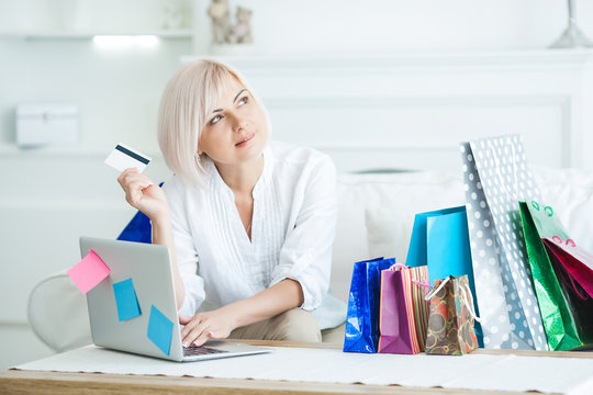 Attractive Mid Adult Woman Doing Online Shoppind. Female Holding Credit Card And Sitting At The Laptop With Shopping Bags Indoors.