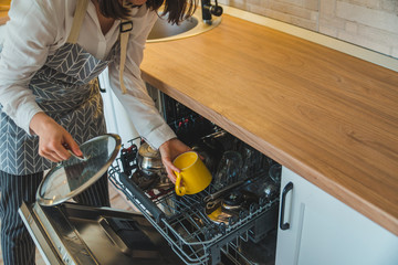 young pretty woman putting dishes in dishwasher