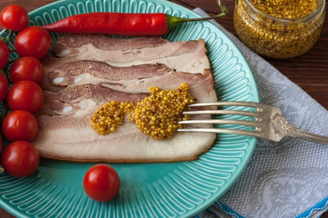 Baked pork belly or bacon sliced into thin slices on a plate with tomatoes, poured with mustard.