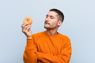 Young caucasian man holding a donut relaxed thinking about something looking at a copy space.