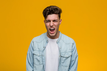 Young handsome student wearing a denim shirt screaming very angry and aggressive.