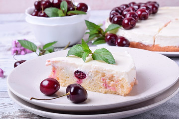 Piece of pie with sour cream and cherries topped with mint on the white plate