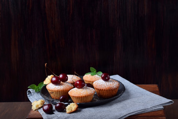 Muffins topped with cherries and sugar powder on the plate against the black background