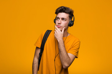 Young cool student man listening to music with headphones standing with outstretched hand showing stop sign, preventing you.