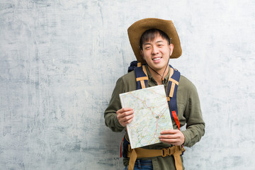 Young chinese explorer man holding a map cheerful with a big smile