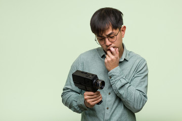 Young chinese man holding a vintage camera relaxed thinking about something looking at a copy space