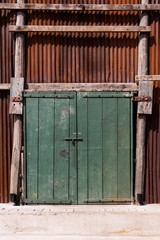 Old green wooden door made of plank on the wall Corrugated zinc fence with old rusty surface brown for the background.