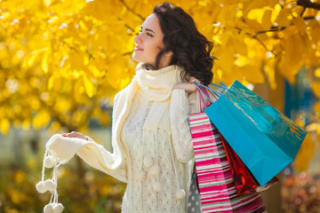 Cheerful young woman doing shopping. Beautiful girl outdoors on the autumn background with shopping bags.