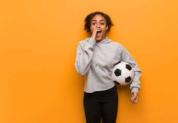 Young fitness black woman shouting something happy to the front. Holding a soccer ball.