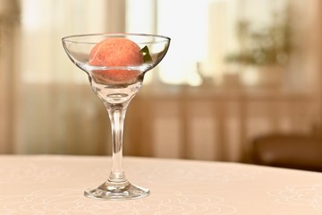 Transparent glass vase with ripe, fresh peach with a leaflet. In the interior, on the edge of the table, against the window.