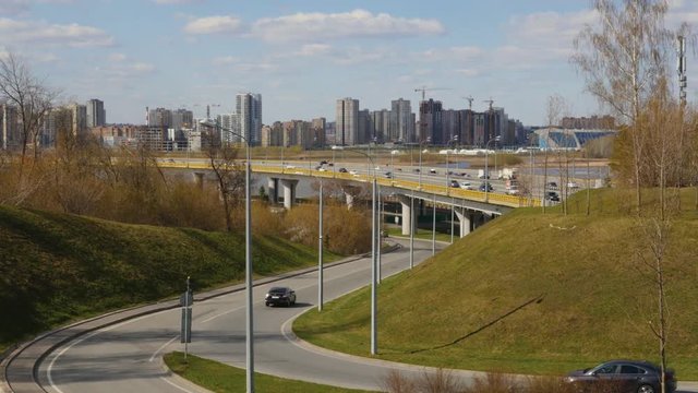 ity traffic near a wide bridge in Kazan city. Cars are moving on the highway and on the bridge. We can see new blocks of high-rise building from the distance. 
