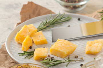Slices of delicious marble cheese with a sprig of rosemary and cheese knife on a plate on a light concrete background. close-up