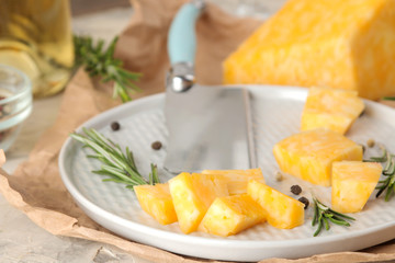 Slices of delicious marble cheese with a sprig of rosemary and cheese knife on a plate on a light concrete background. close-up