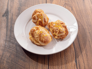 Three eclair on a white plate with sugar sweet syrup. Plate is on a wooden table.