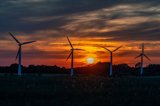 four wind turbines on a field against a golden sunset