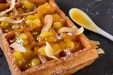 A large Viennese waffle cooked at home is on a black background and filled fruit sauce