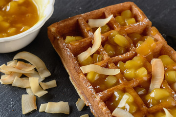 A large Viennese waffle cooked at home is on a black background and filled fruit sauce