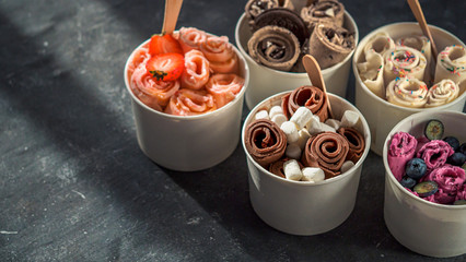 Rolled ice cream in cone cups on dark background. Different iced rolls or Thai style rolled ice...