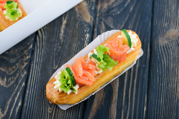 Tasty and beautiful eclairs on a wooden board. Appetizing dessert with red fish, cucumber, cheese and greens.