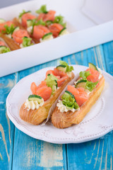 Tasty and beautiful eclairs on a wooden blue board. Appetizing dessert with red fish, cucumber,...