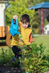 European boy is helping his parents to water the trees in the garden. © Artem