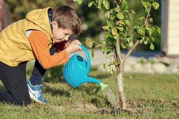 European boy is helping his parents to water the trees in the garden.